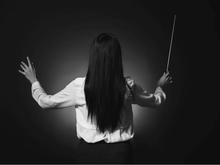 Black and white photo of female conductor from behind with hands raised.