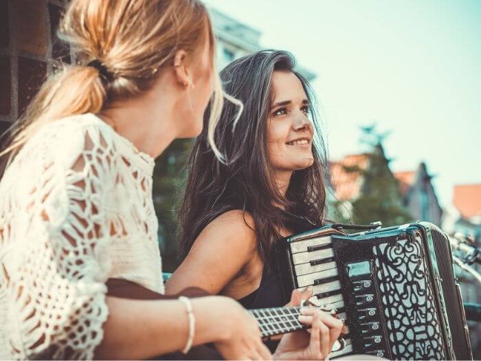 Two young female street musicians, one playing acoustic guitar and the other an accordian.