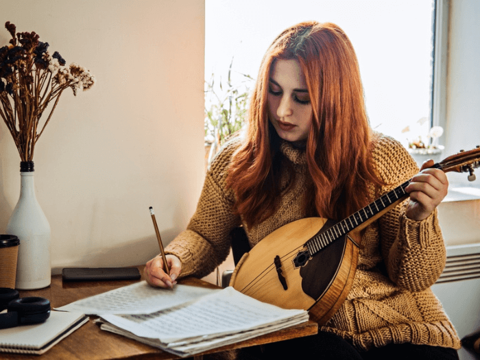 Young woman playing Mandolin at home while writing music.