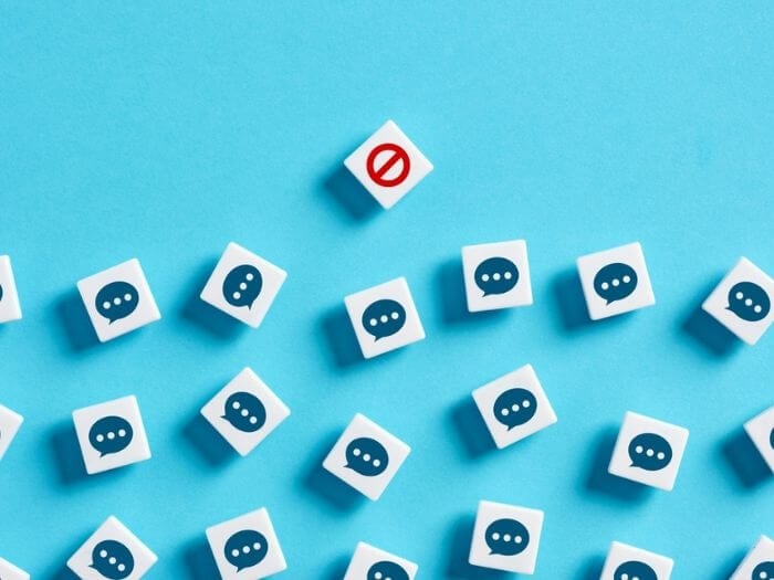 Wooden blocks with speech bubble graphics on them against a blue background, a single block with a red stop sign is in front of them, blocking the line, representing free speech restrictions.