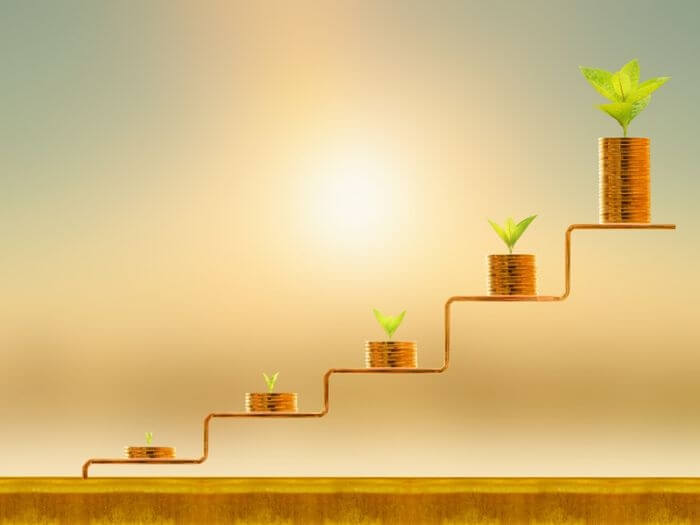 Stacked gold coins and plants on a step, growing with each incline against a sunlight background. Investment and saving money concept.