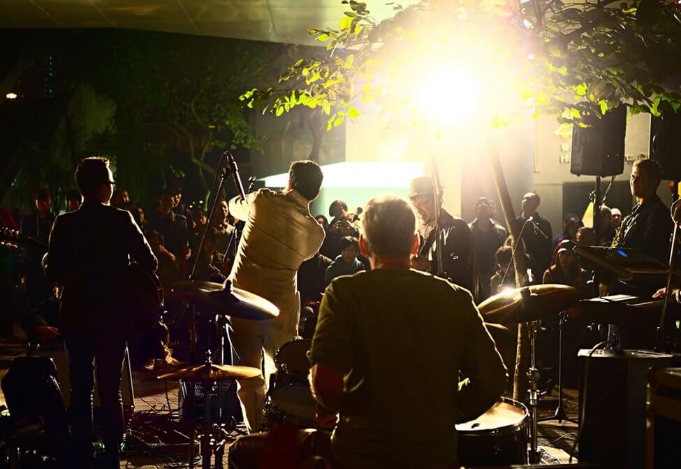 Band performing to a crowd in the evening, on a small outdoor stage.