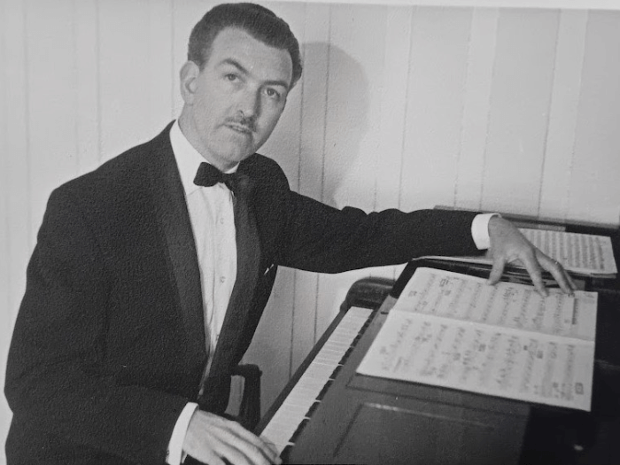 Black and white image of Gil sat at a piano in his younger years.