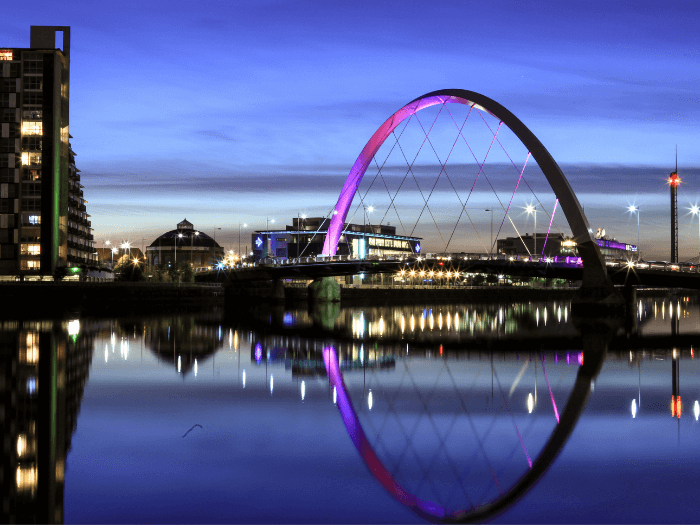 River Clyde, Glasgow at Night towards the Squinty Bridge which is lit in purple and reflected in the water beneath.
