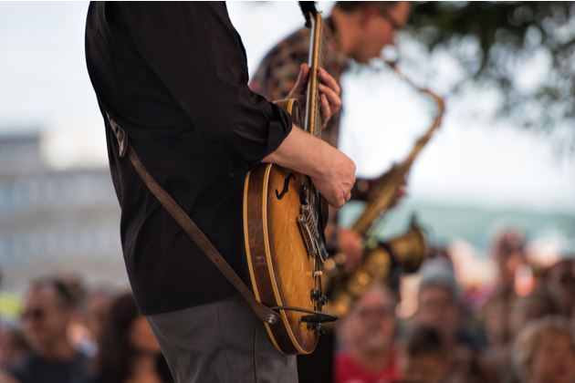 Photograph of a guitarist and saxophonist performing to an outdoor audience.