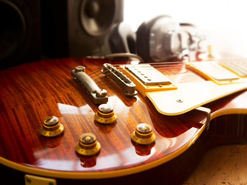 Photograph zoomed in to the volume dials on an electric guitar, with the sun shining brightly on the polished wood.