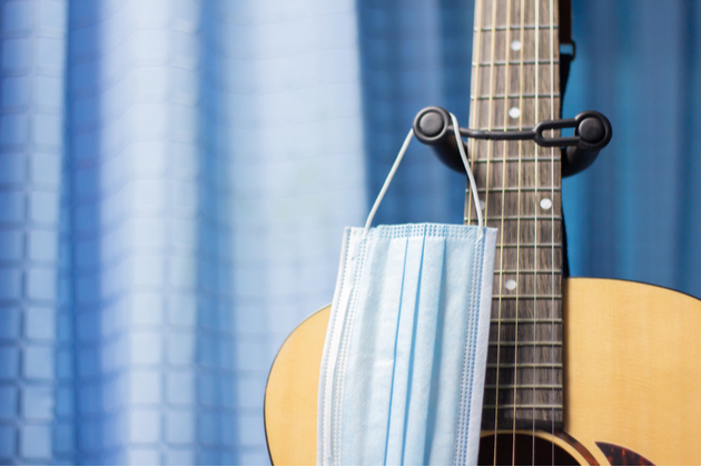 Photograph of a guitar with a mask hanging from the neck, a blue curtain in the background.