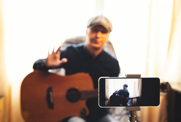 Photo of guitarist setting themselves up for a video being recorded on a camera phone