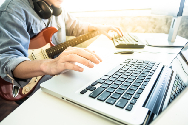 Photograph of person sat at a computer with their guitar set up to play.