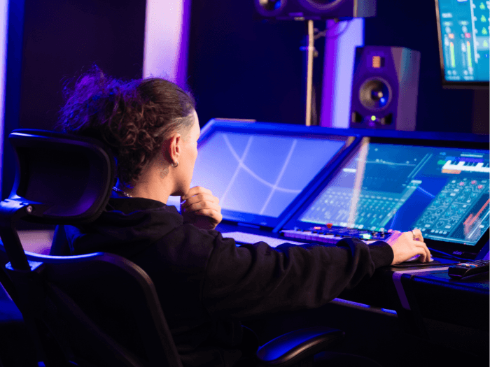 A person sitting at a digital audio workstation in a recording studio.