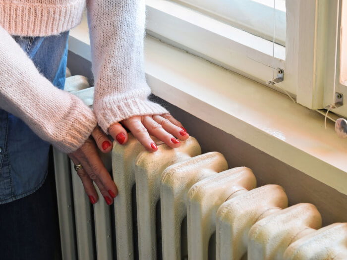 A person is pressing their hands against a radiator with an open window beside them