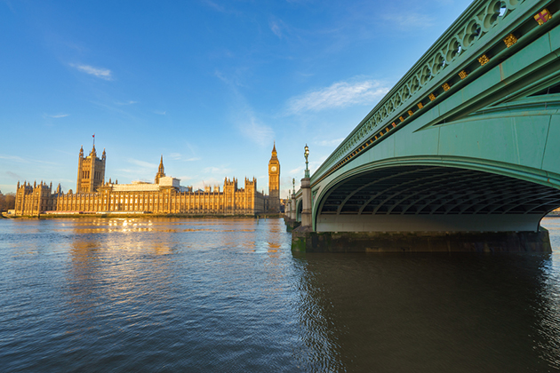 Photograph of the houses of parliament, viewed from across Westminister bridge and the Thames on a bright, blue day.