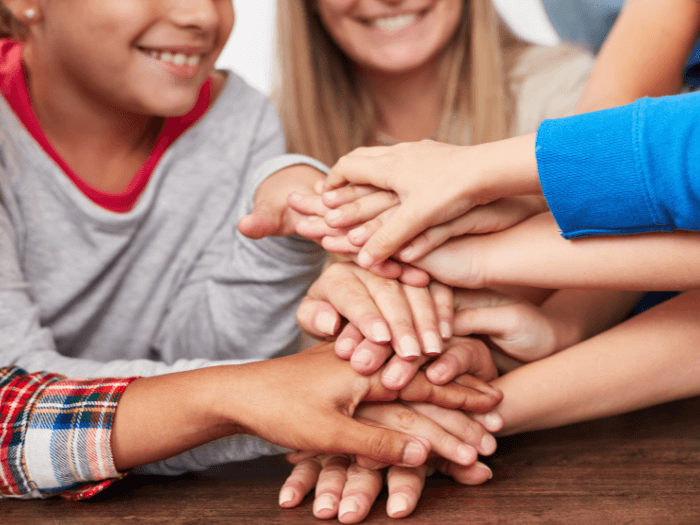 Close up of a mix of children stacking hands, representing inclusion and teamwork.