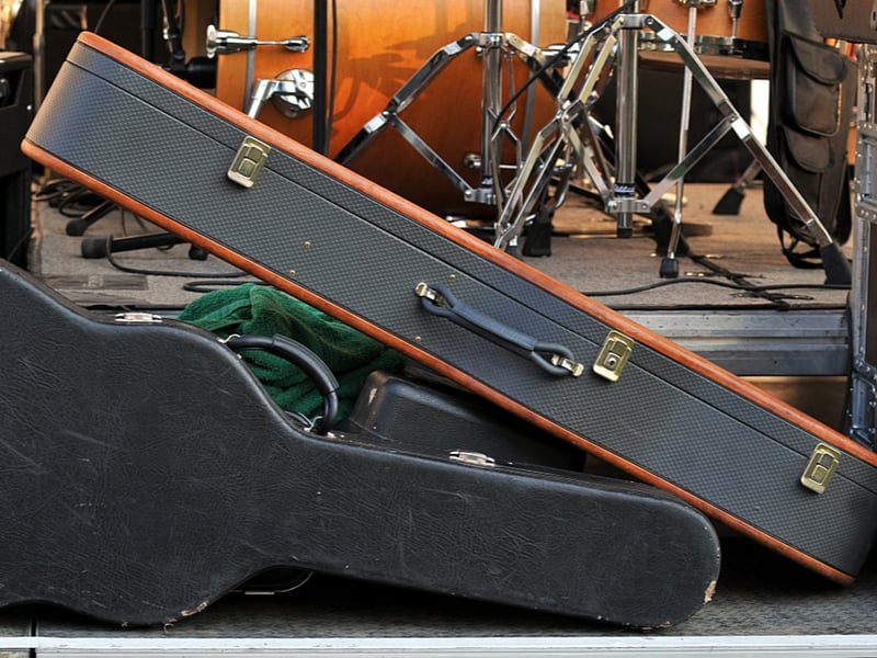 A number of instruments in hard cases proped at the side of a stage, looking slightly chaotic.