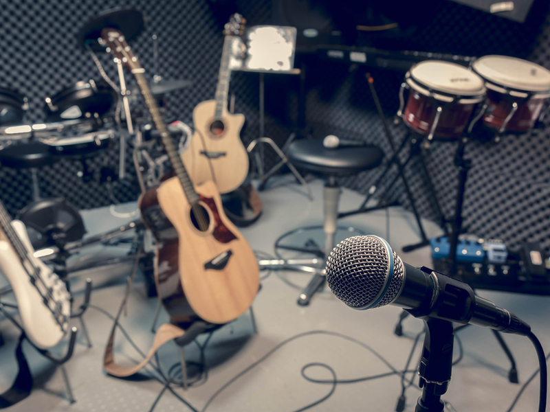 A selection of instruments set up in a studio, including two acoustic guitars, an electric guitar and a microphone.
