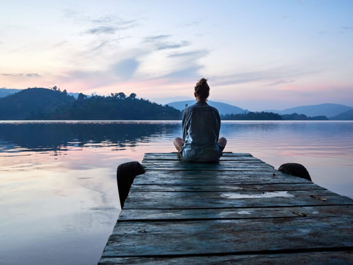 Quiet figure sits at the end of a dock, watching a sun rise over a body of water.