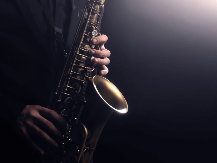 Close up of Saxophonist's hands holding instrument while playing jazz music on dark stage.