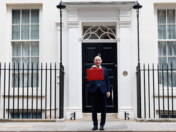 Chancellor of the Exchequer John Healey dressed in a dark navy suit, holding the red budget brief case outside of 11 Downing Street.
