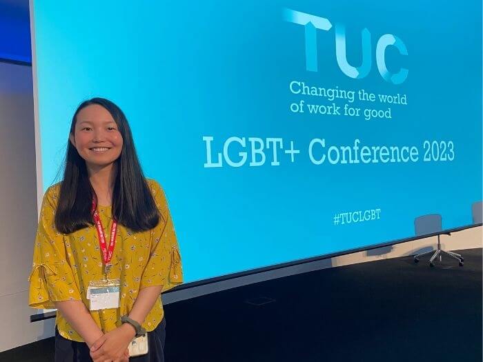 Utako Toyama smiling in front of a blue presentation screen saying TUC LGBT+ Conference 2023.
