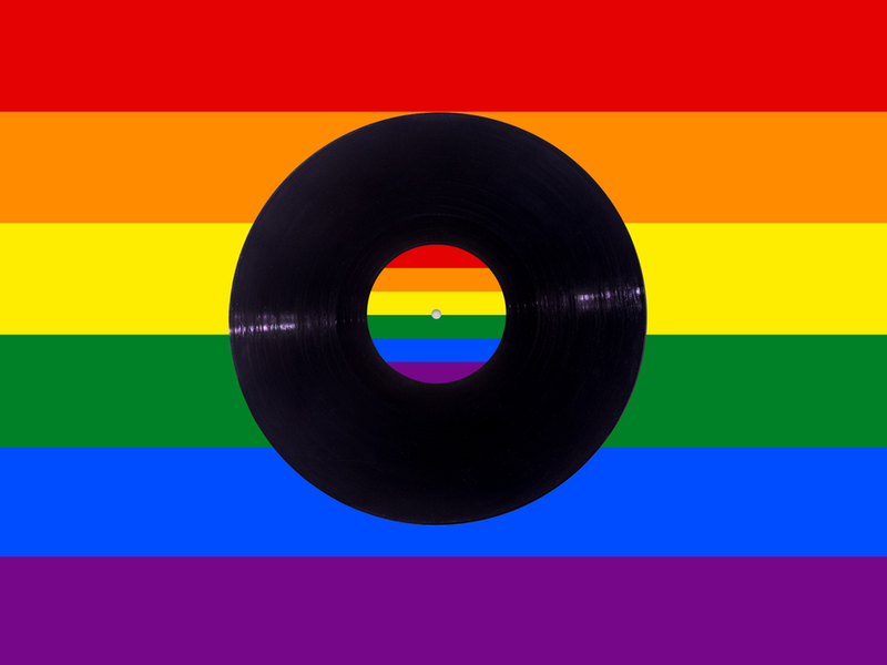 Photograph of a vinyl record with the LGBT+ Pride flag coloured stripes behind it