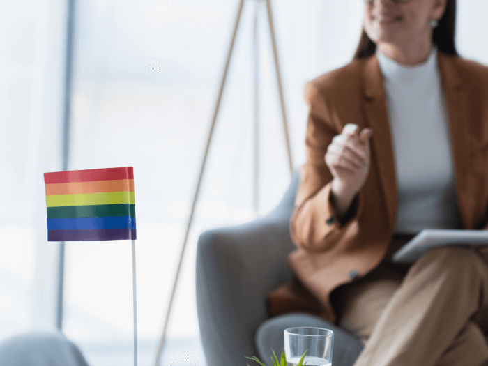 Small LGBT+ flag near cropped psychologist with digital tablet on blurred background.