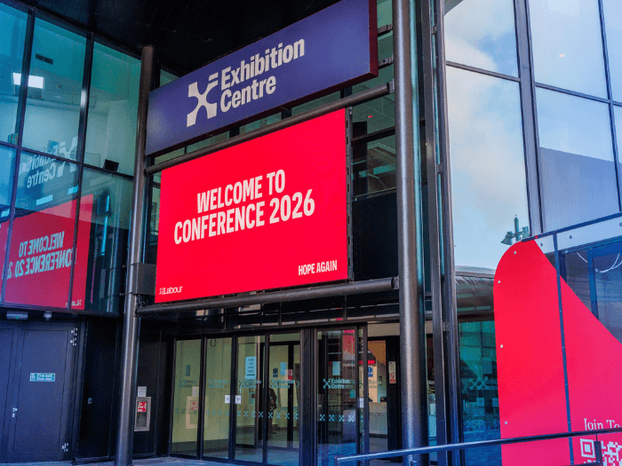 Exterior shot of the entrance to the main exhibition hall at Conference. There is a big, bright red, digital sign above the door saying 