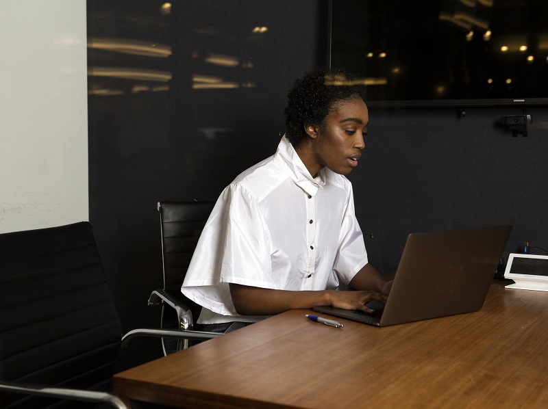 Photograph of a person using a laptop working at a table in an office.