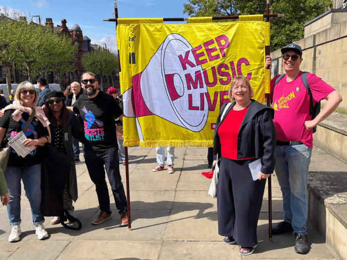 MU members and staff standing in front of the Union's bright yellow marching banner which reads 