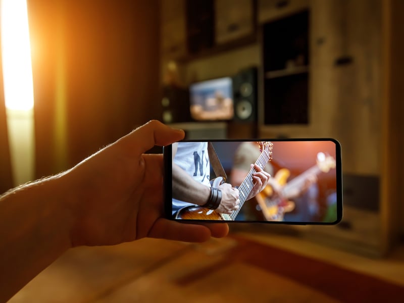 Photograph of a person watching a live streamed gig on a mobile phone in their house.