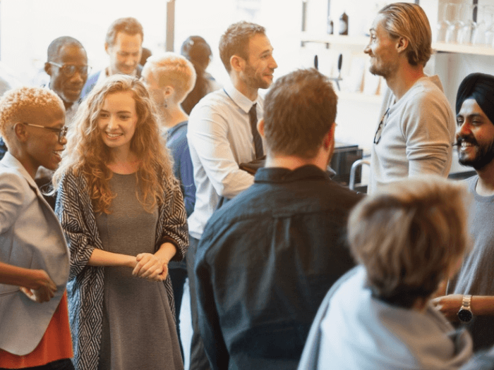 A diverse group of people, dressed smart/casual, smiling and networking.