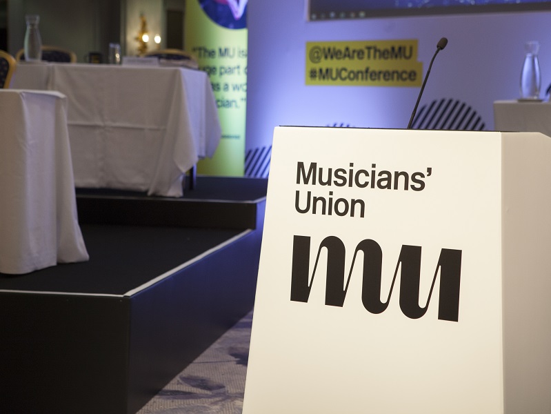 Photograph from the MU Conference in 2019, focusing on a large white speakers podium with 