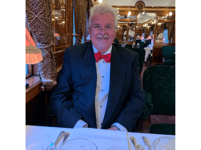 Martin, sat at the table of a formal dinner, dressed in a suit, smiling.