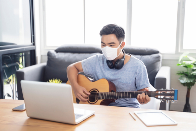 Man in a mask playing guitar in front of a laptop