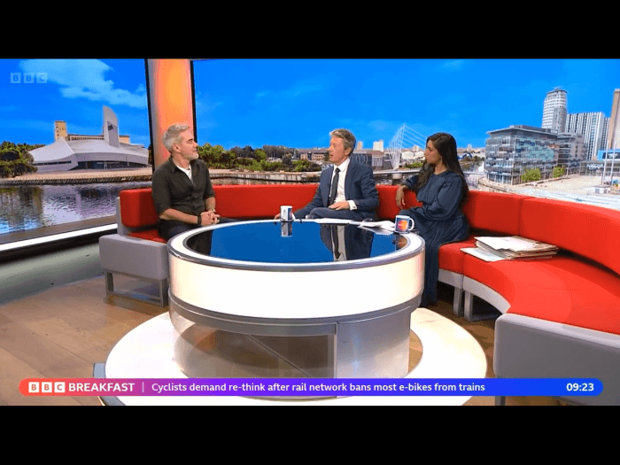 Three people sitting on a long sofa being filmed for BBC Breakfast.