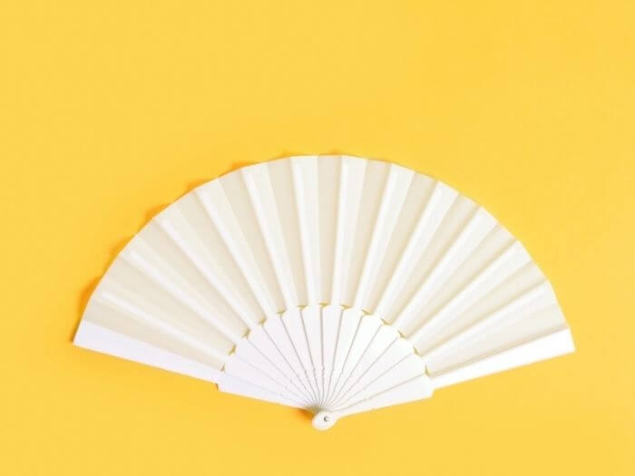 White hand fan on yellow background, top view, concept of hot flush and the menopause.