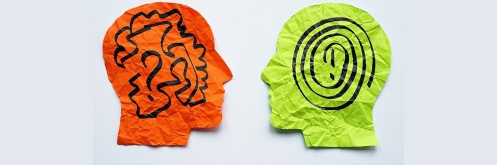 Two pieces of paper, one orange and one green, cut into the shape of a head. They are facing each other, one with a question mark and squiggles, and the other with a smooth spiral and exclamation mark