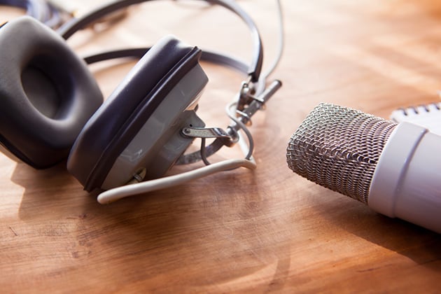Photograph of earphones and a microphone lieing on a sun soaked wooden desk.