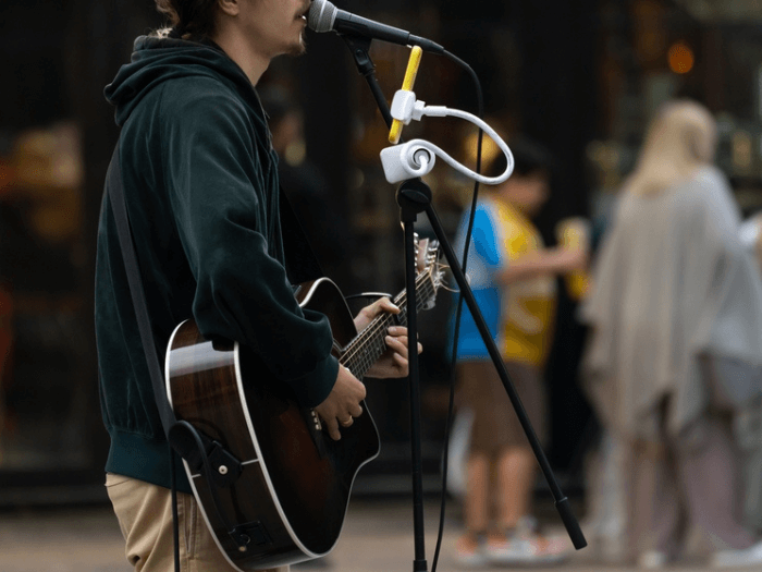 Close up of male musician busking on the street, playing an acoustic guitar and singing into a microphone.