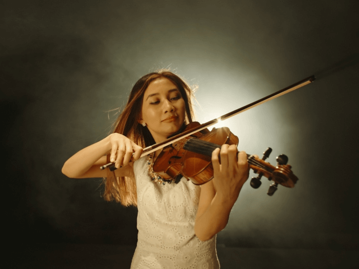 Female violin player performing under a spotlight on a dark stage.