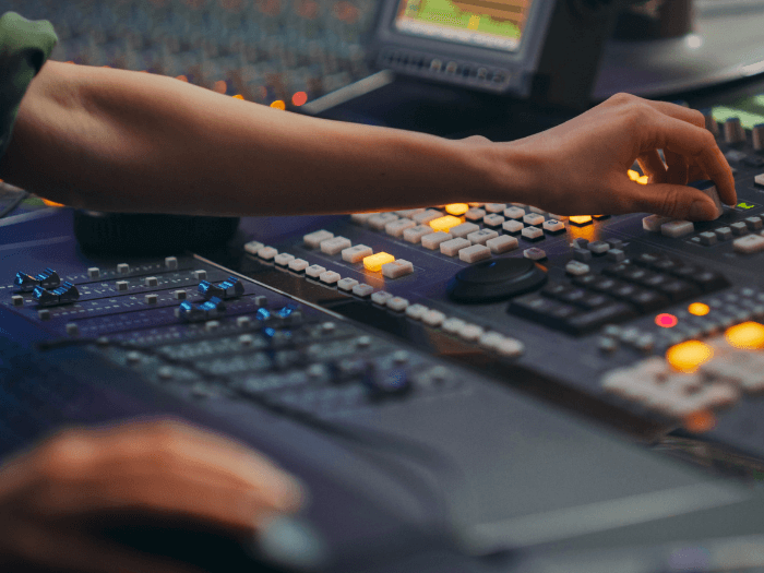 Hands touching sound mixing desk buttons.