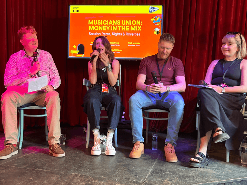 The panellists sat on the stage with microphones, in front of a screen with saying 
