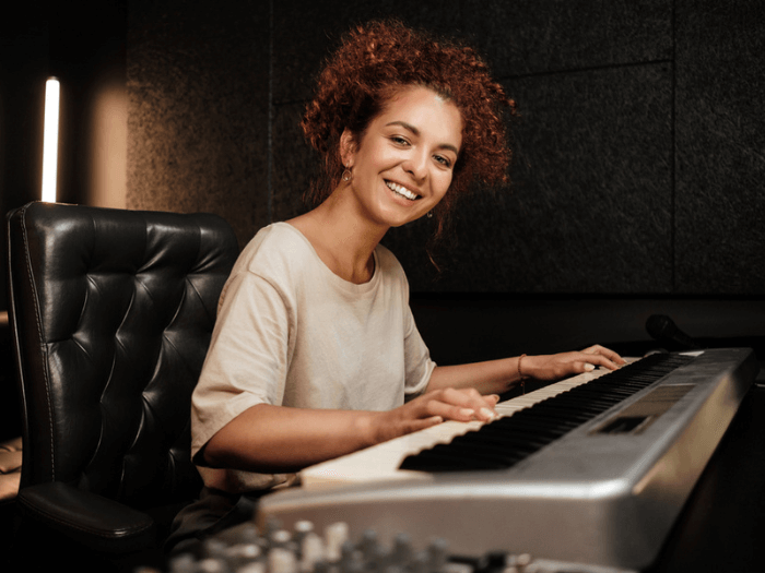 A young female musicians playing an electric piano in a recording studio.