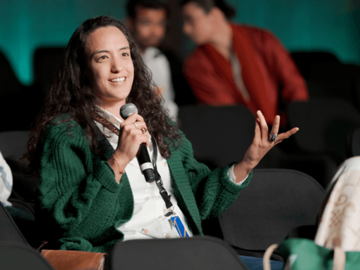 A young woman in the audience of a panel. holding a microphone and gesturing.