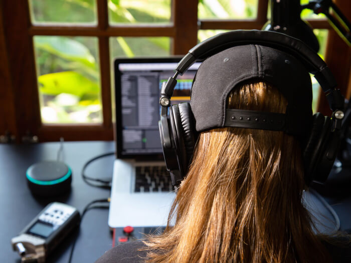 Person sat in front of an open laptop wearing headphones and programming music.