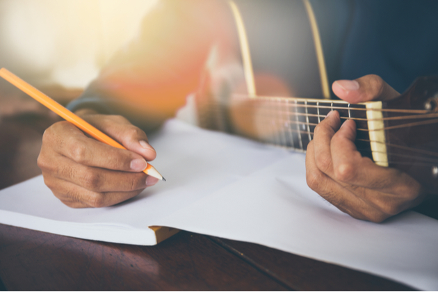 Photograph of a person holding a guitar and writing in a notebook
