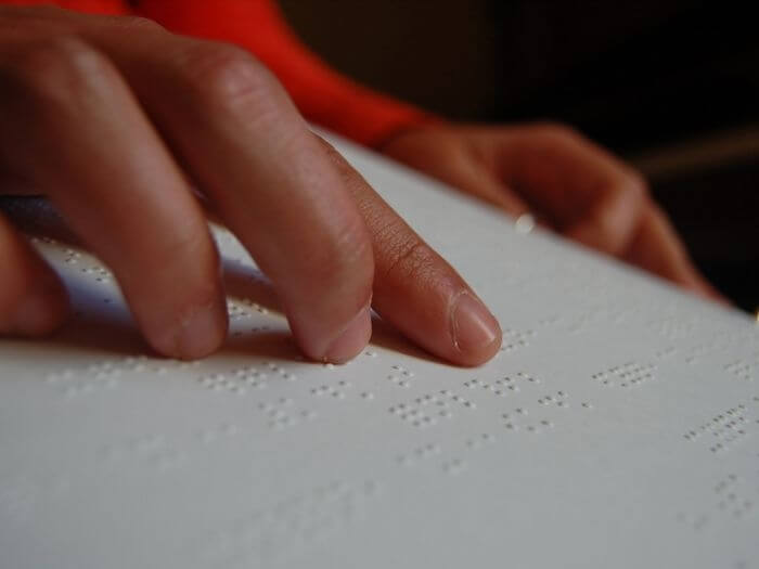 A hand reading music notation in a braille book filled with sheet music.