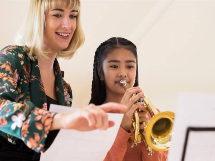 Music teacher points at a score as a child looks and plays on a trumpet