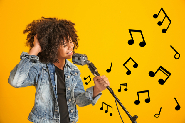 Photograph of a young girl, singing into a microphone. The background of the picture is a yellow block of colour, with graphics of different musical notes flying out and away from the girl.