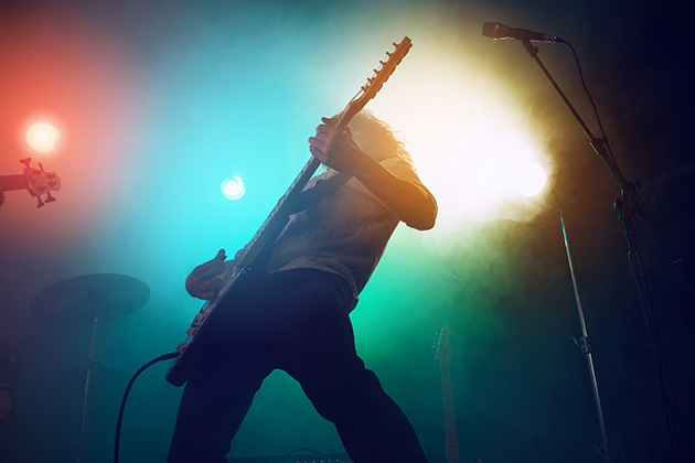 Silhouette of man on stage playing electric guitar, lit up back lights