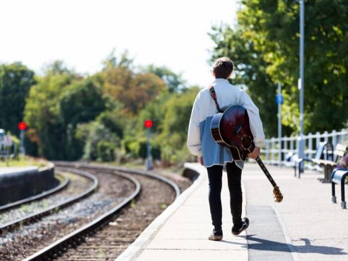 A young musician with an acoustic guitar following the train tracks in Woodbridge, Suffolk